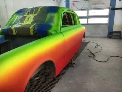Colorfully painted classic car body in a workshop, with green, blue, yellow, and red spray finish
