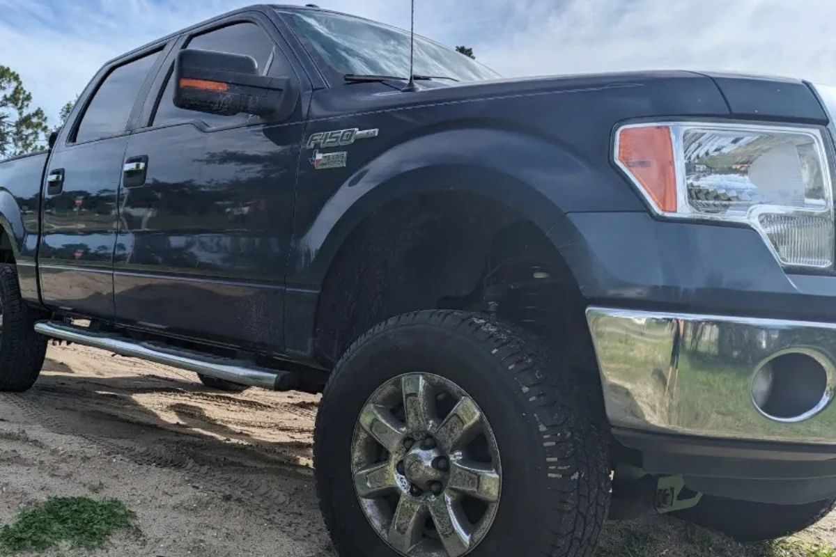 Black Ford pickup truck parked on a sandy roadside under a cloudy sky