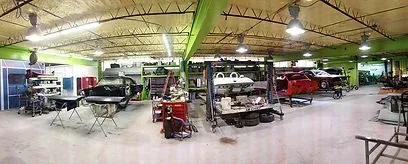 Wide indoor garage with several classic cars and work tables under bright ceiling lights