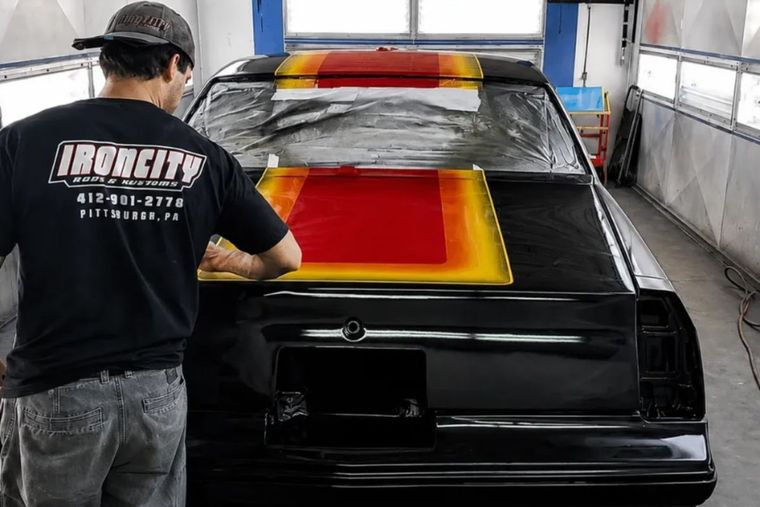 Painter spraying red and yellow stripes on a black car in a paint booth