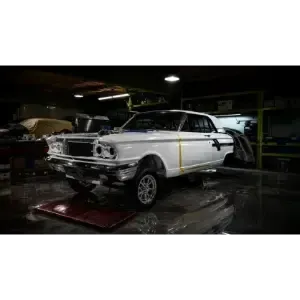 White classic car in a dim garage, parked on a lift with front-end repairs in progress
