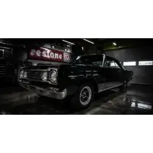 Classic black car displayed in a dim garage, with chrome details and a glossy floor reflection
