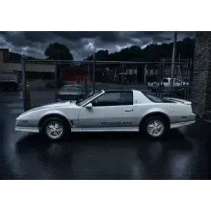 Silver sports coupe parked on a wet street, side view, with dark cloudy sky and fenced lot behind it