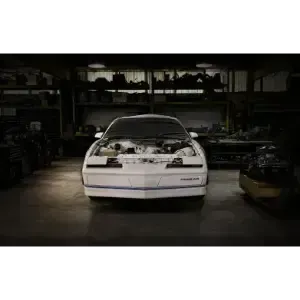 White sports car in a dim garage, front view with the hood open and engine exposed
