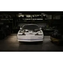 White sports car in a dim garage, front view with the hood open and engine exposed