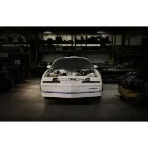 White sports car in a dim garage, front view with the hood open and engine exposed