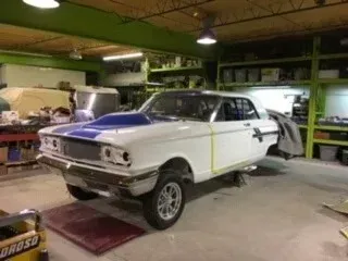 White classic car in a garage, partly disassembled on a lift with tools and equipment nearby