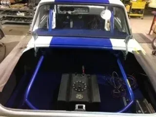 Blue-and-white car with an open rear compartment showing installed audio equipment and wiring