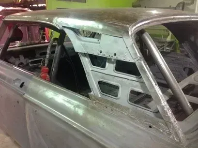 Primered classic car body with a stripped interior and exposed roll cage in a garage