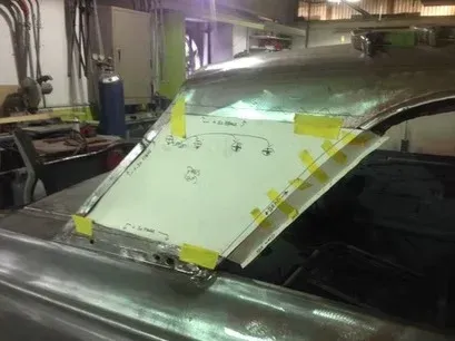 Car body panel being fitted in a workshop, secured with yellow tape and marked with alignment notes