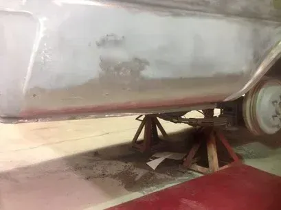 Silver vehicle on wooden jack stands in a garage, with a red floor and concrete wall.