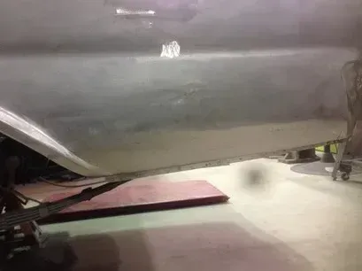 Low-angle view of a gray car raised on a lift in an auto repair shop.
