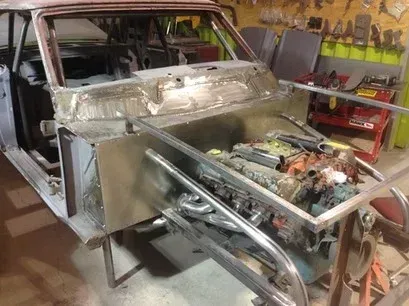Classic car in a garage with a stripped body and exposed engine bay during restoration