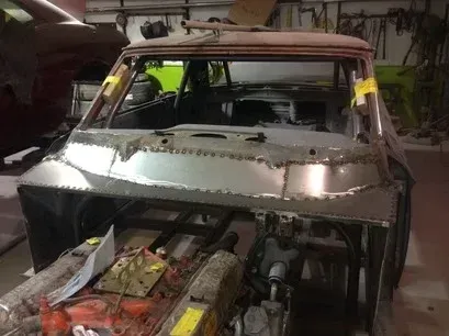 Partially stripped car in a garage with exposed engine and metal bodywork under repair