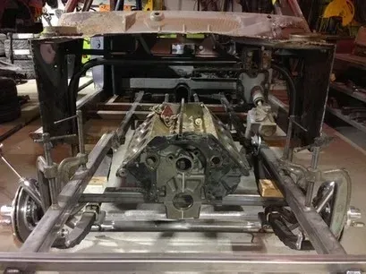 Exposed car chassis with engine and suspension components in a workshop, viewed from the front.