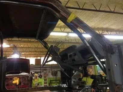 Large vehicle chassis lifted in a garage, with mechanics working underneath under bright lights
