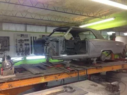Classic car body on a lift in an auto body shop, partially disassembled and under repair.