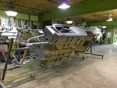 Large industrial machine or vehicle chassis in a workshop, tilted on a metal frame under green lighting