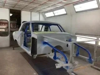 Partially assembled blue car body in a workshop, with exposed frame and body panels.