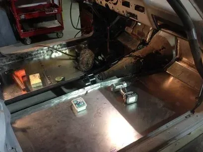 Car interior with exposed floor panels and two small electronic modules on the metal floor.