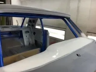 Blue car body shell in a garage, showing the interior and roof frame during restoration