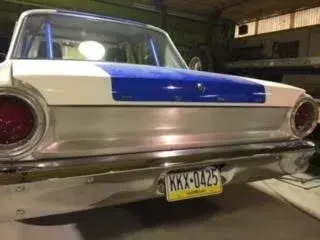 Rear view of a classic car with a blue trunk panel and yellow license plate in a garage