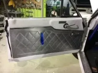 Car door panel with gray diamond quilting and a blue pull strap, viewed in a workshop.