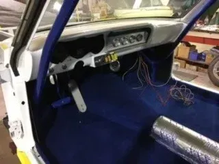 Car interior stripped for repairs, with blue race seat, exposed wiring, and bare floor panels