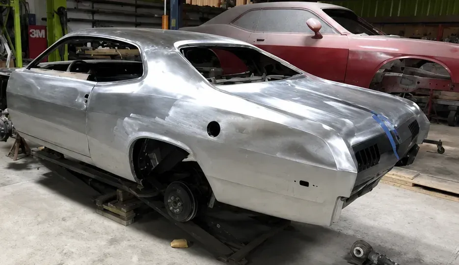 Silver classic car body shell in a workshop, with a red car in the background
