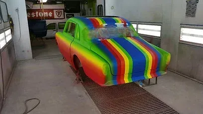 Rainbow-painted car in a spray booth, covered in bright rainbow stripes and colors.