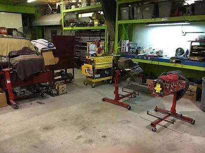 A cluttered garage workshop with tools, a workbench, and two engine stands on a concrete floor