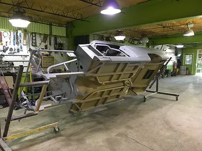 Large metal machine in a green workshop, tilted on support stands with tools and equipment nearby