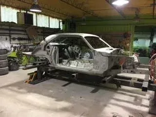 Silver car body on a frame machine in an auto repair shop, with tools and tires in the background