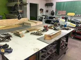 Workshop table cluttered with tools, wood pieces, and supplies in a workshop.