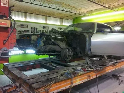Silver car on a lift in an auto repair shop with its front end disassembled