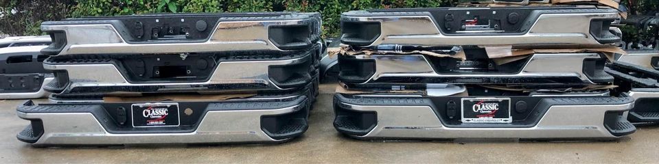 Two stacks of chrome bumpers are sitting on top of each other on the ground.