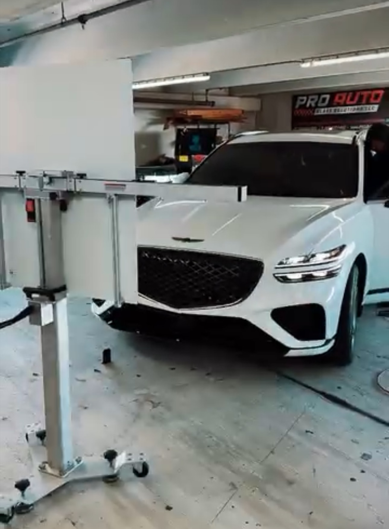 A man is installing a black rooftop cargo box on a black car in a garage. He is wearing gloves and working on the roof.