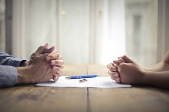 Hands clasped on a table with a divorce document and pen. Window in background.