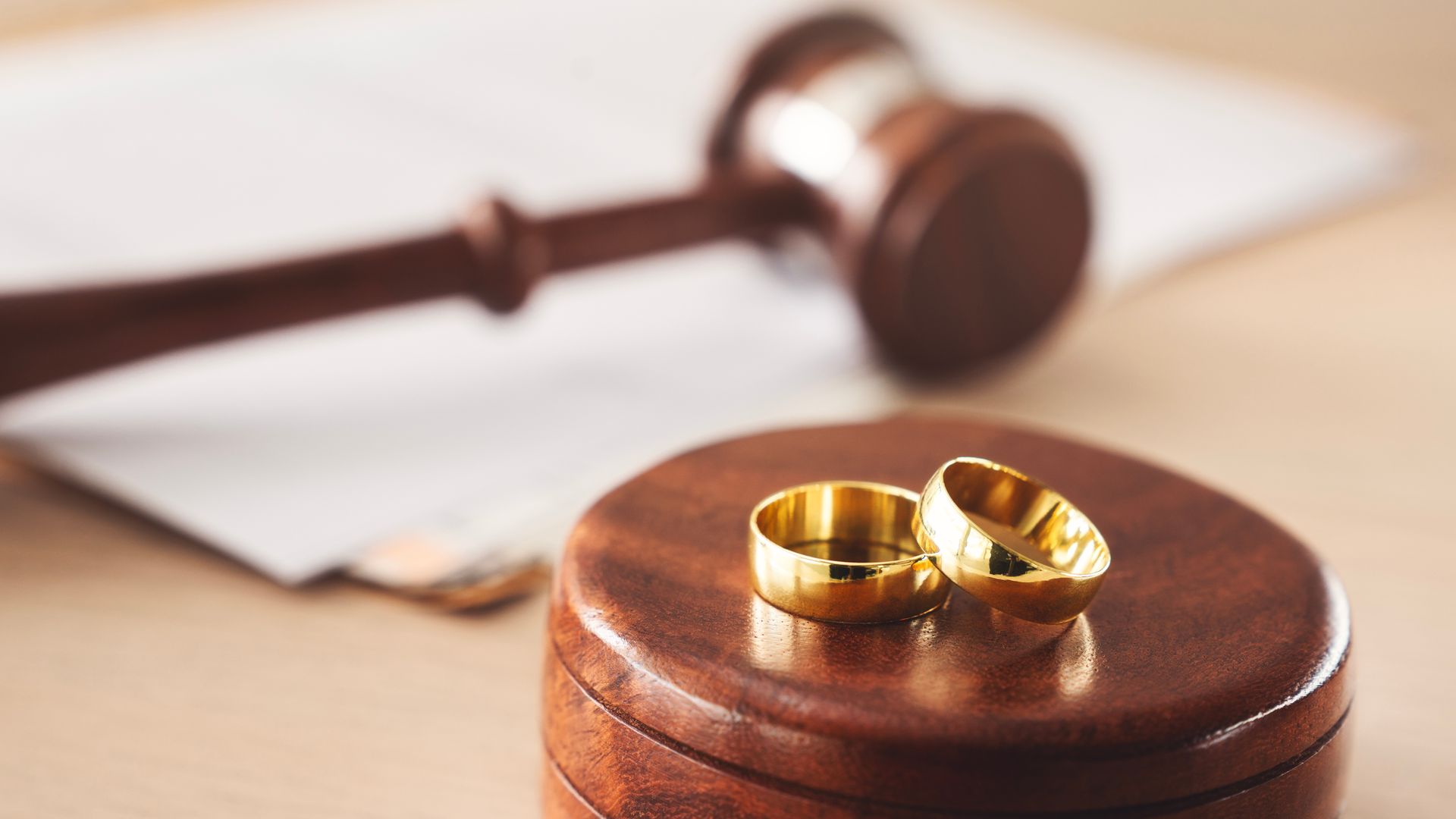 Photograph showing two gold wedding rings placed on a wooden judge's gavel block,