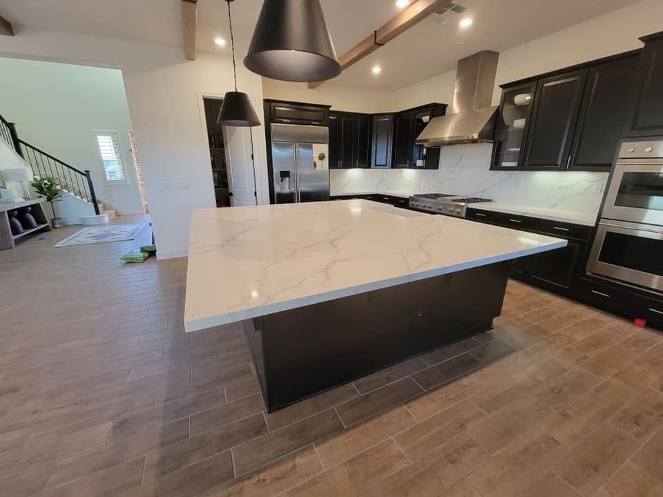 Modern kitchen with a large white island, dark cabinets, and wood-look tile flooring