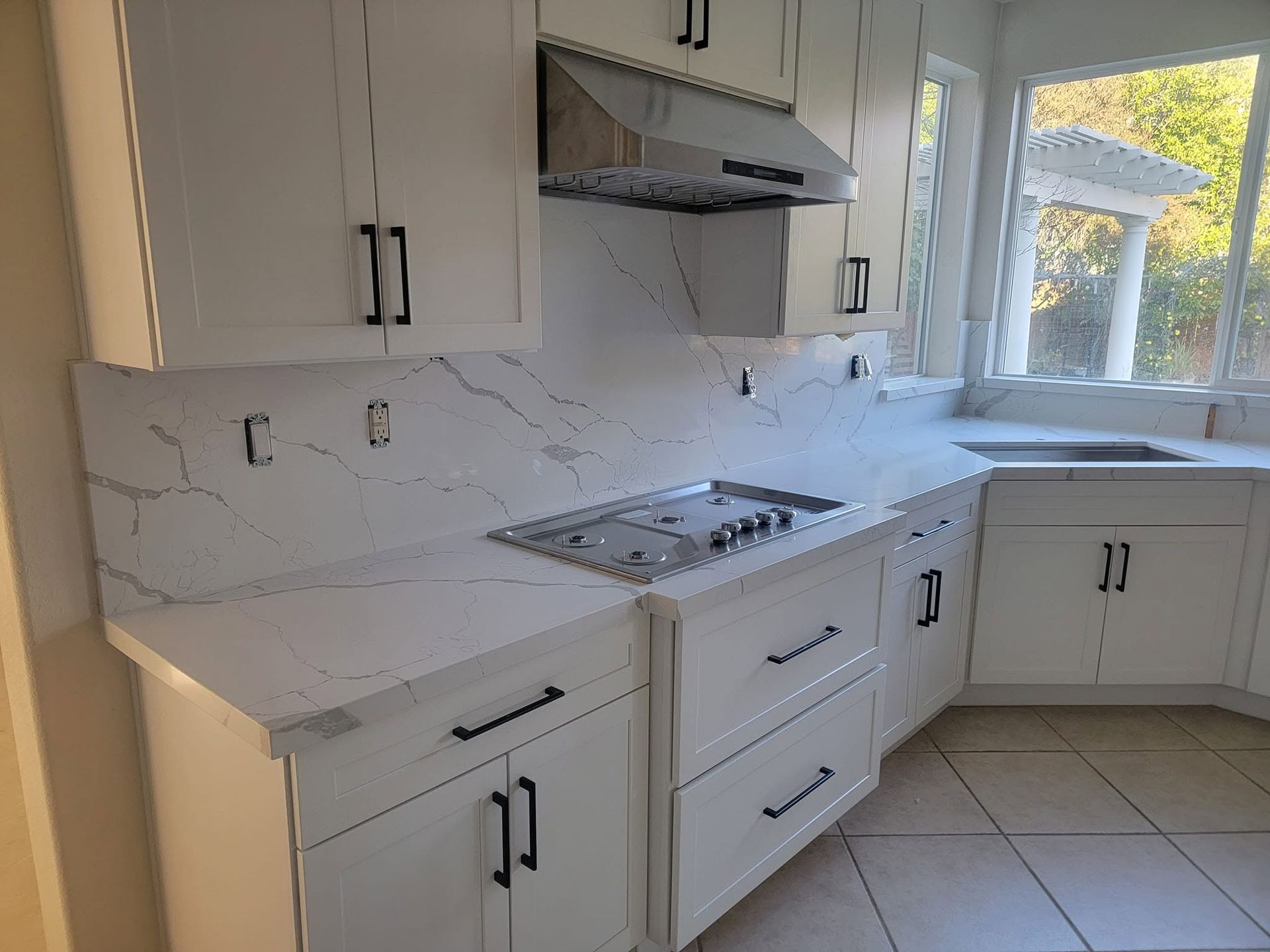 White kitchen with cabinets, marble backsplash, stove, range hood, and tiled floor by a bright window