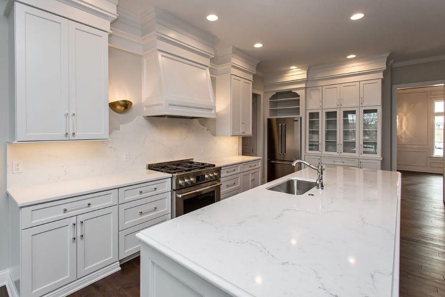 Bright white modern kitchen with large island, stainless steel appliances, and glass-front cabinets