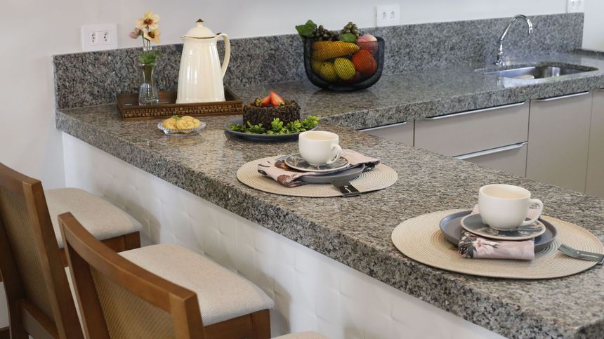 Granite kitchen island set with decorative plates, cups, fruit bowl, and bar stools