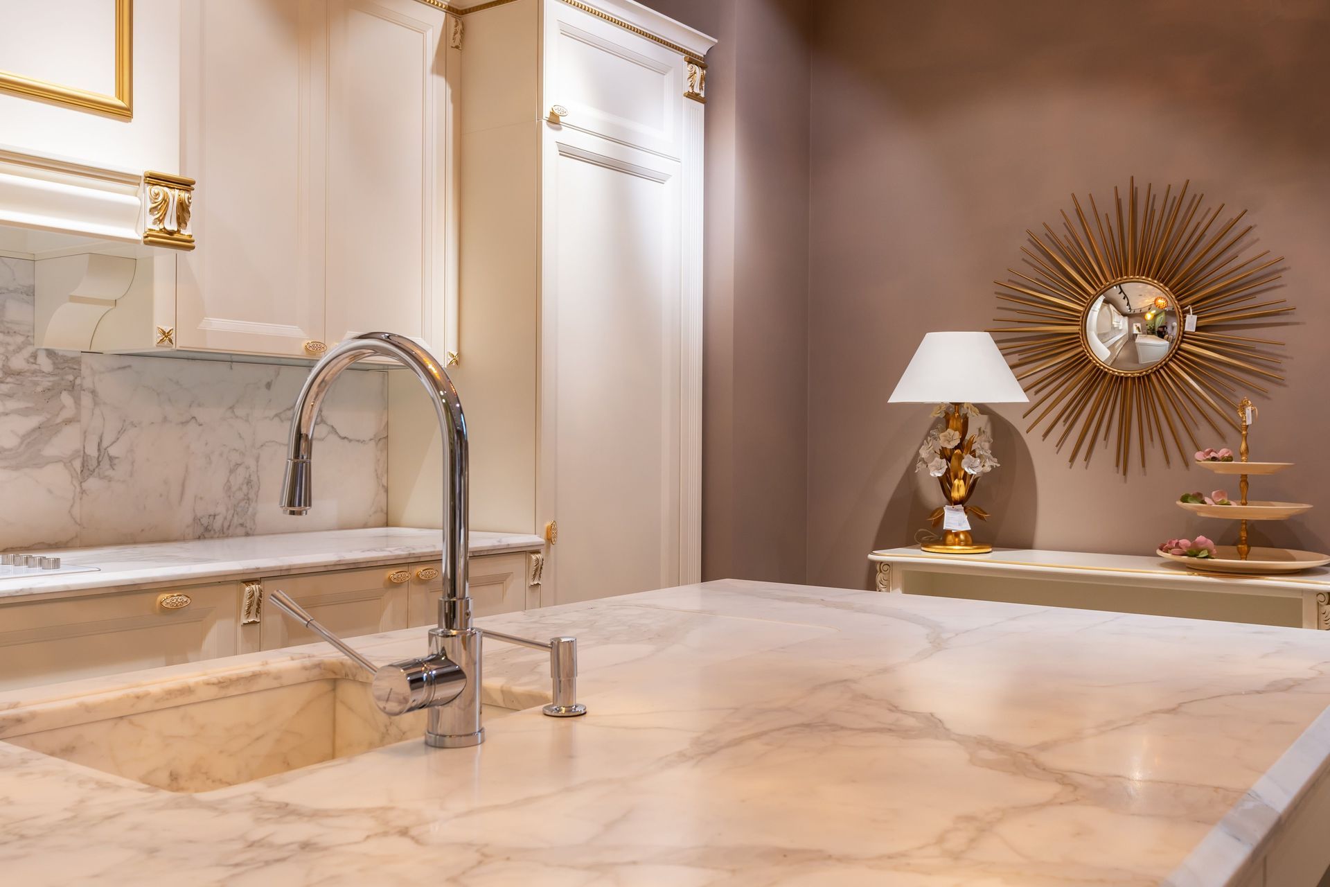 Luxury marble kitchen with gold accents, chrome faucet, and decorative lamp on the counter