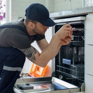 Technician inspecting an open dishwasher, leaning in with a tool in a kitchen.