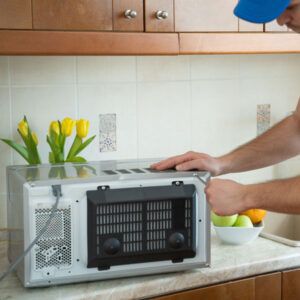 Man putting a microwave on a kitchen counter beside yellow flowers and a bowl of fruit