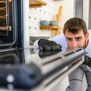 Person aiming a shotgun inside a kitchen, viewed through the barrel, with a focused expression.
