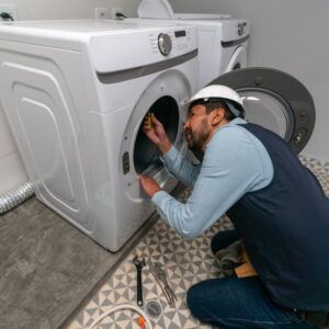 Technician repairing a front-loading washing machine with tools in a laundry room
