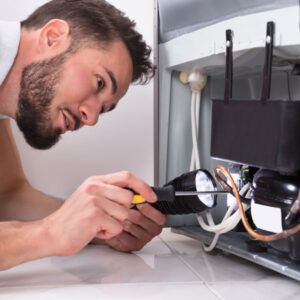 Technician using a flashlight and screwdriver to inspect wiring inside an appliance or cabinet