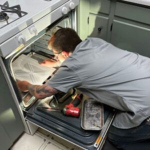 Person repairing an open kitchen appliance with tools inside a built-in cabinet.